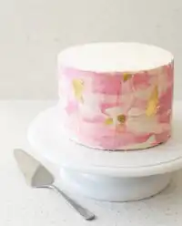 A Two-Layer Watercolor Buttercream Cake with blue and green swatches on a white stand.