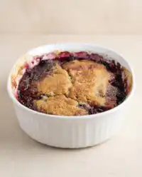 A golden brown blackberry cobbler dump cake bubbling in a square ceramic baking dish.