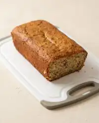 A golden loaf of Cake Mix Banana Bread resting on a rustic wooden cutting board in a farmhouse kitchen.