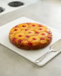 A golden brown cast iron skillet pineapple upside down cake cooling on a rustic wooden table.