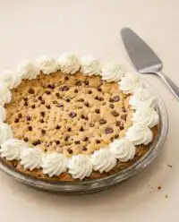 A thick and chewy classic chocolate chip cookie cake decorated with chocolate buttercream swirls on a vintage plate.