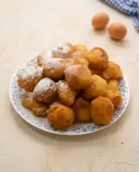 A mountain of golden Classic Funnel Cake Bites dusted heavily with sweet powdered sugar
