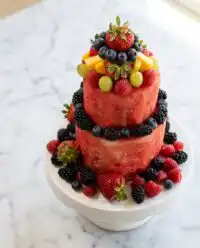 A two tiered Classic Watermelon Fruit Cake decorated with fresh strawberries kiwis and blueberries