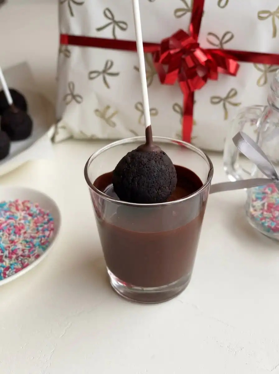 Demonstrating how to dip brownie cake pops into a mug of smooth melted chocolate candy coating