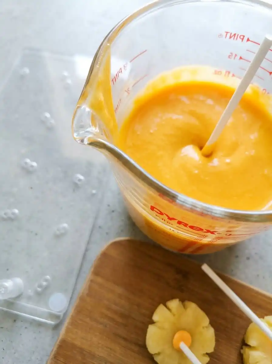 A hand dipping Classic Pumpkin Cake Pops into smooth orange candy coating