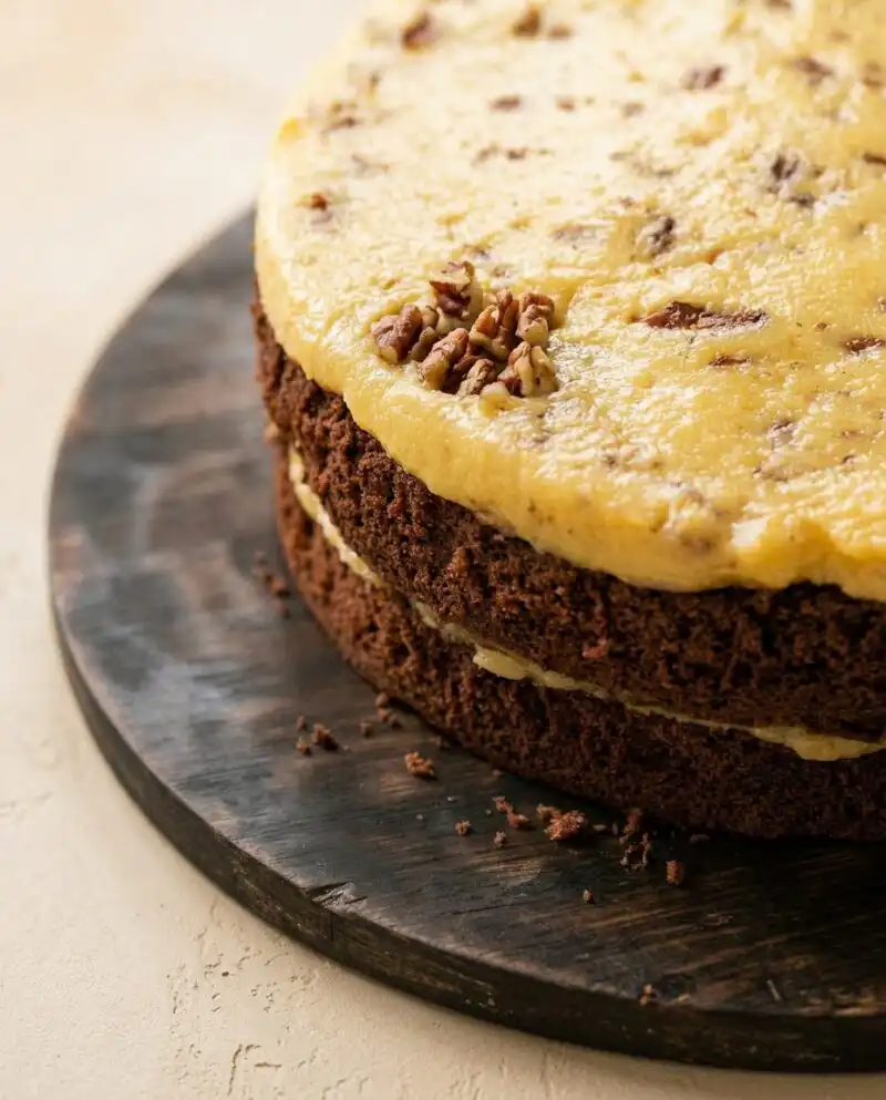 A completed German Chocolate Cake with layers of coconut pecan frosting on a serving stand.