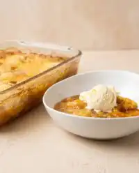 A freshly baked Cinnamon Canned Peach Dump Cake with a golden brown crispy crust in a glass baking dish.