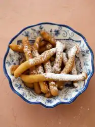 A golden brown serving of Cinnamon Sugar Funnel Cake Fries tossed in spiced sugar in a basket.