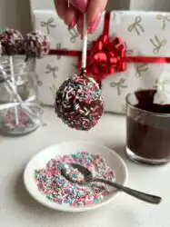 Deliciously fudgy brownie cake pops decorated with white sprinkles resting on a white platter
