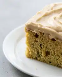 A sliced zucchini cake with cinnamon and nutmeg topped with cream cheese icing and walnuts.