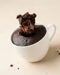 A warm rustic Nutella Mug Cake sitting on a dark wooden countertop with a linen towel.