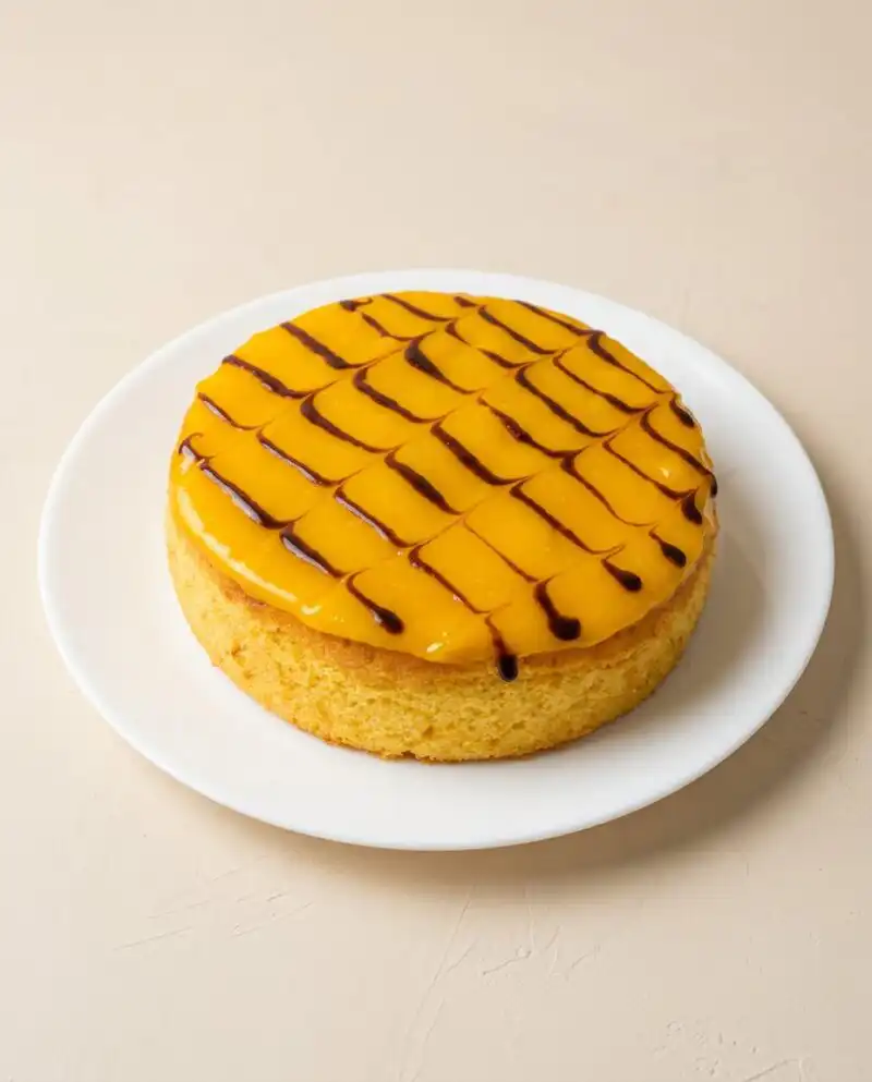 A rustic Mango Fresh Fruit Topped Cake sitting on a black metal wire cooling rack.