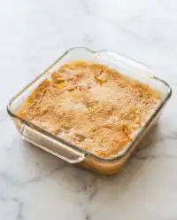 A warm slice of Peach Dump Cake with Frozen Peaches served on a plain white plate with vanilla ice cream.