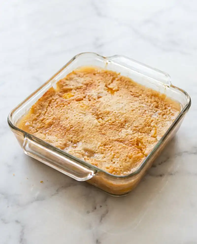 A warm slice of Peach Dump Cake with Frozen Peaches served on a plain white plate with vanilla ice cream.