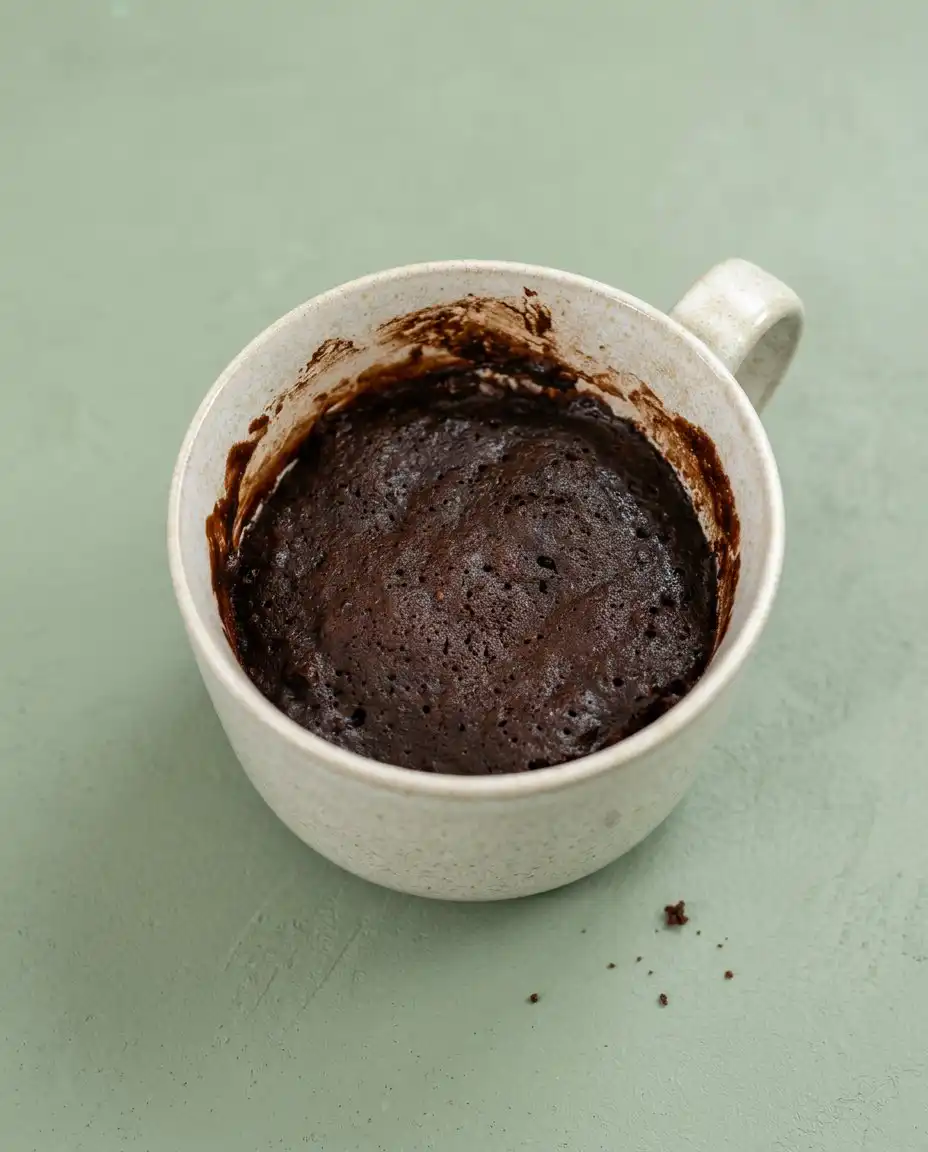 Serving a rich Chocolate Mug Cake topped with cool whipped cream and served with a vintage spoon.