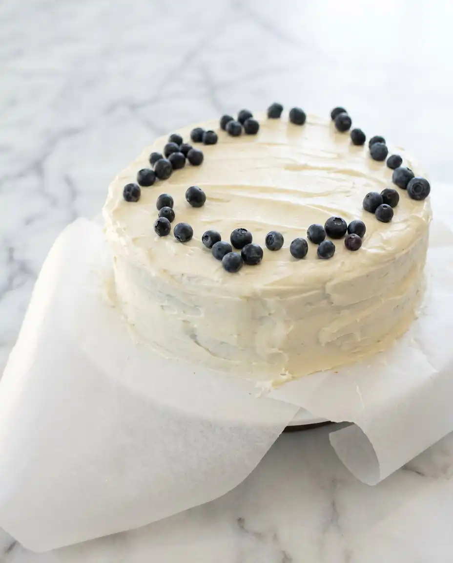 Classic Blueberry Layer Cake 16 A slice of Classic Blueberry Layer Cake on a plain plate next to a fork and linen towel.