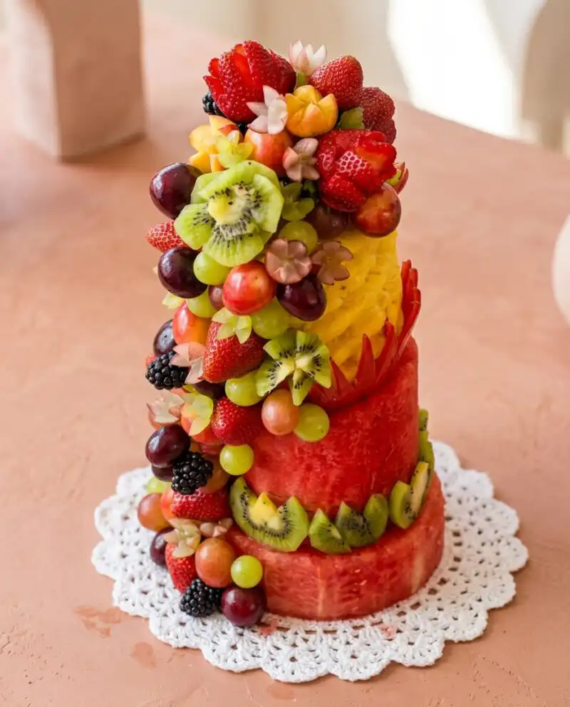 A two tiered Watermelon Fruit Cake Tower decorated with fresh berries and sliced kiwi