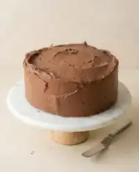 A rich and fudgy One-Bowl Chocolate Zucchini Cake cooling on a wooden rack in warm kitchen light.