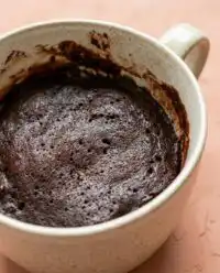 A warm Chocolate Mug Cake resting on a rustic farmhouse table with a linen tea towel.