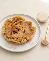Warm cinnamon sugar funnel cake bites piled high on rustic parchment paper in a farmhouse kitchen.